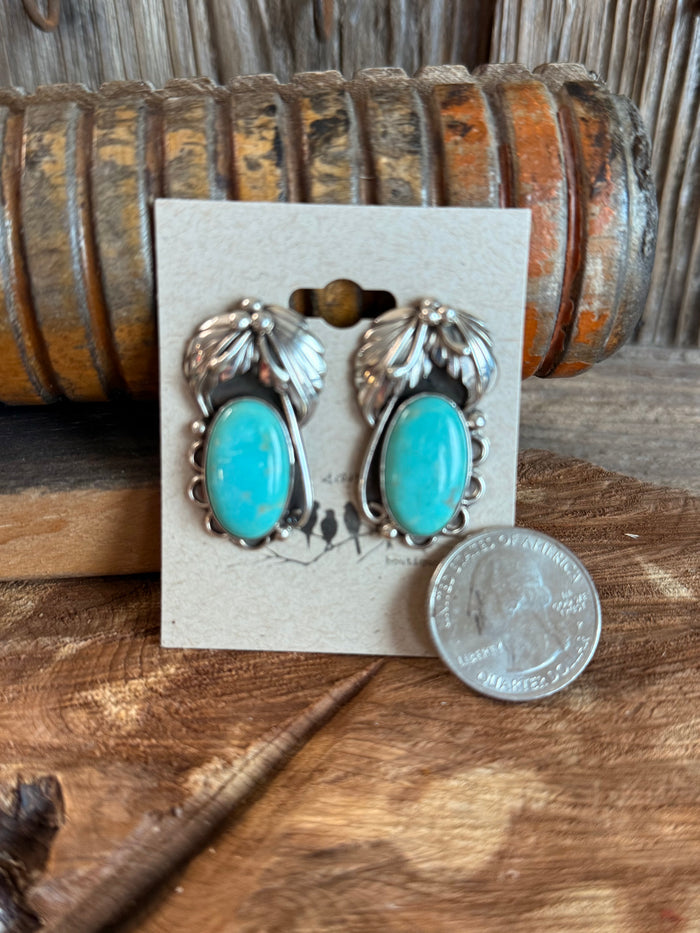Turquoise oval stud earrings in sterling silver feathered settings, shown with coin