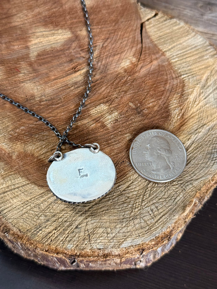 Round pendant charm necklace with engraved metal disc and dark chain, toggle rings.
