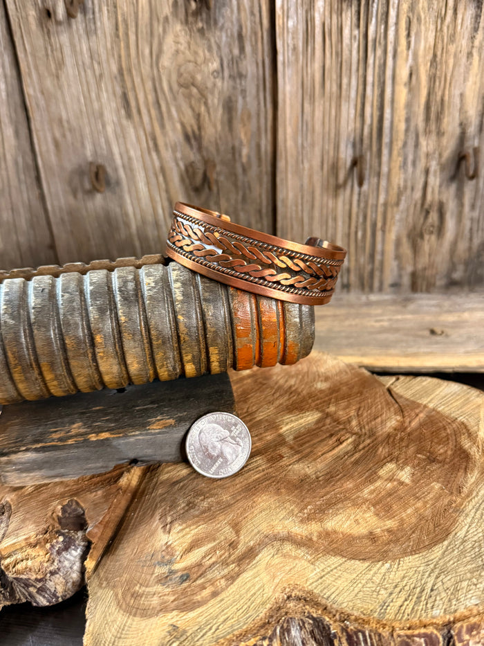 Woven copper cuff bracelet with braided wave engraving, shown with a coin for scale