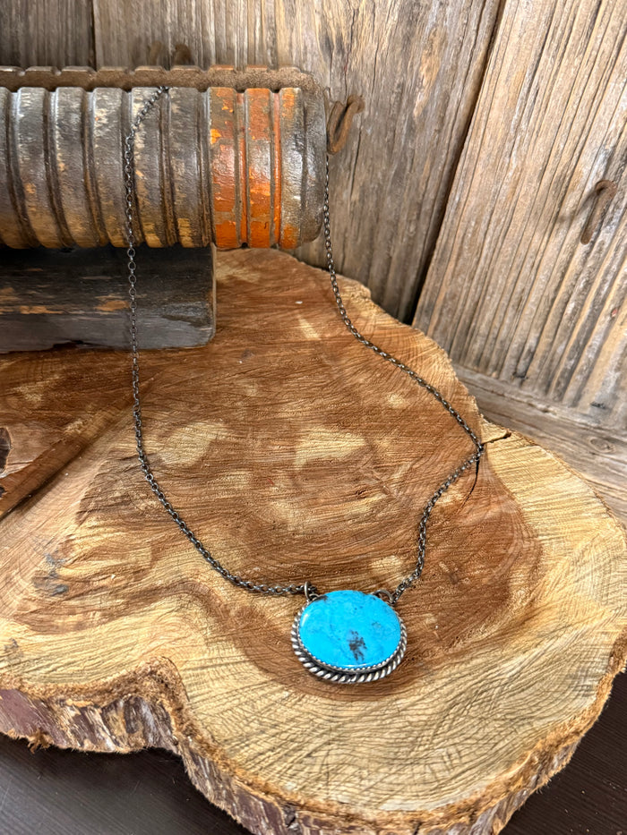 Turquoise pendant necklace with oval blue stone in silver bezel, dark chain.