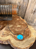 Turquoise pendant necklace with oval blue stone in silver bezel, dark chain.