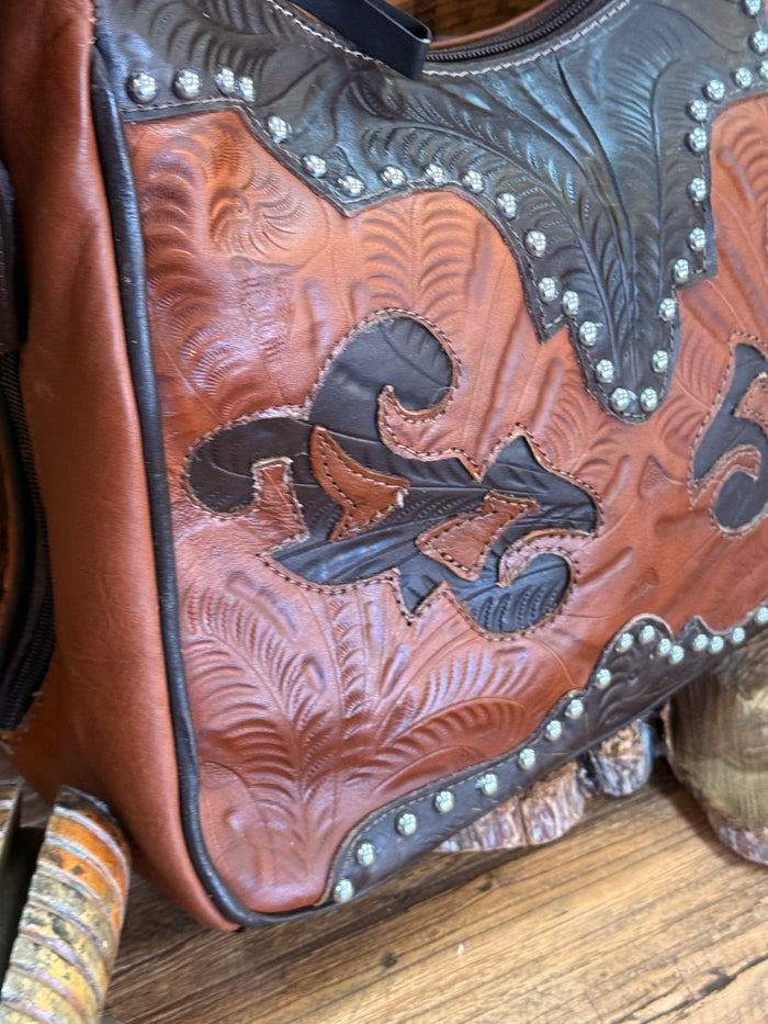 Close-up brown leather handbag panel with floral tooling, silver studs, and black trim
