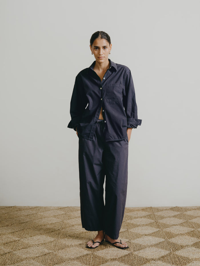 Person wearing a navy blue outfit standing on a patterned carpet with a plain wall background