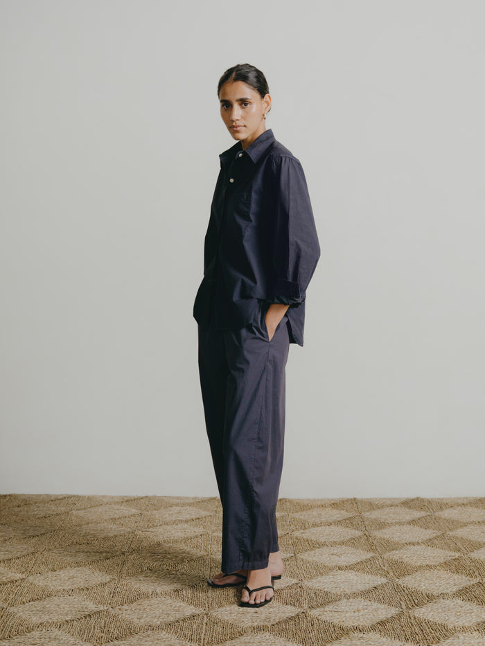 Person wearing a dark outfit standing on a patterned carpet with a plain wall background