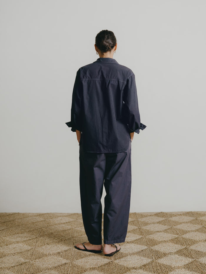 Person wearing a dark blue outfit standing on a patterned carpet with a plain wall background