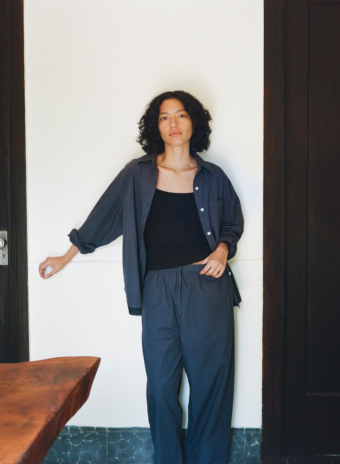 Woman wearing a navy outfit standing against a white wall.