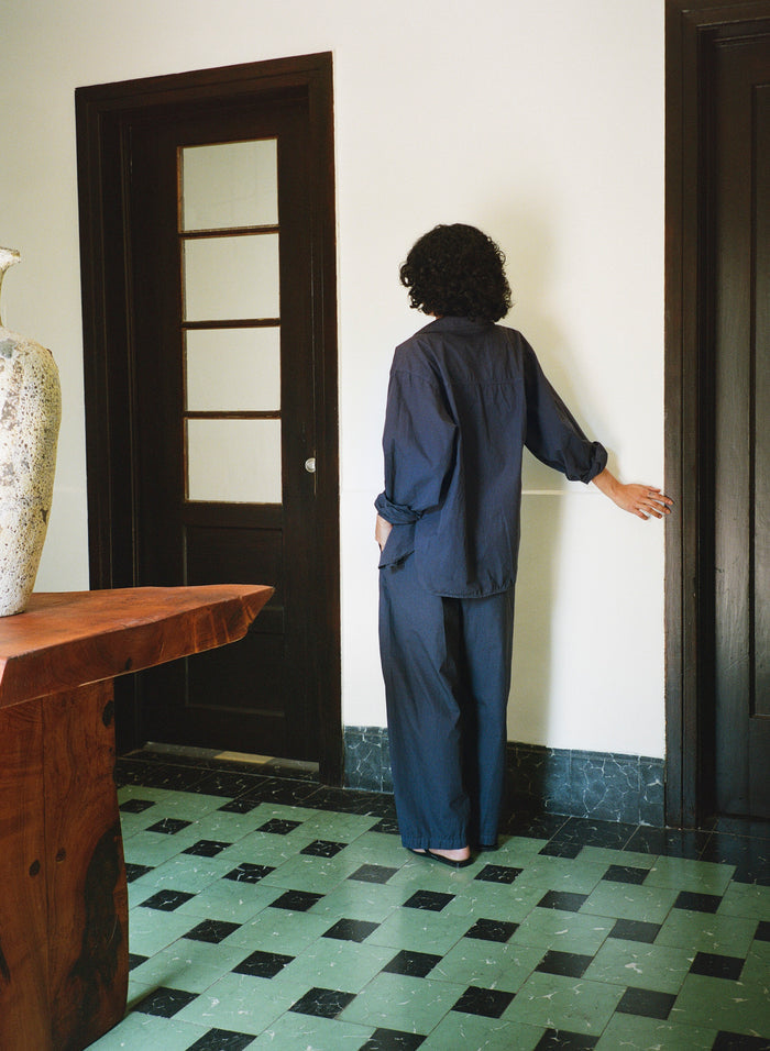 Person in a blue outfit standing in a room with a checkered floor and wooden furniture.
