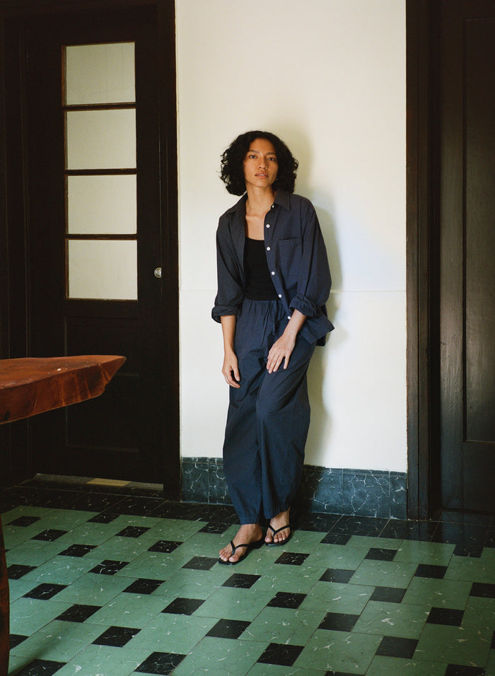 Woman in a navy outfit standing against a white wall with a black door.