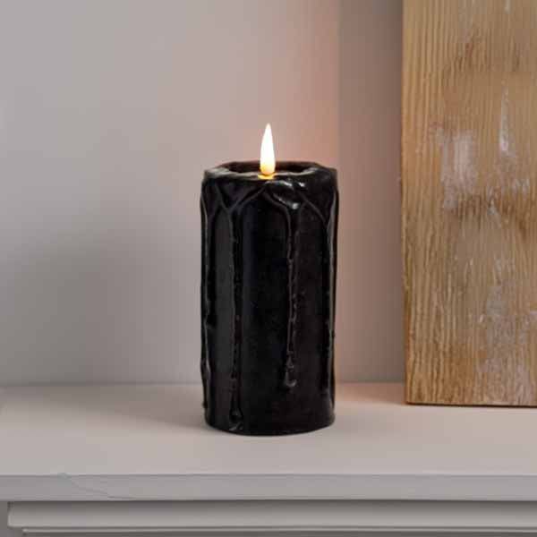 A Battery-Operated Black Candle from Available for Pick-Up & Delivery with a flickering flame adds eerie elegance on a light surface, its textured wax drips exuding sophistication next to an emerging beige accent, perfect for Halloween decor.