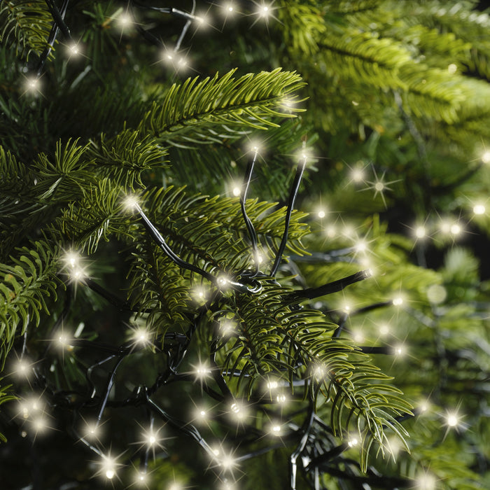 The Cluster LED 1128 ct. String Lights in Warm White from Available for Pick-Up & Delivery illuminate green pine branches with a festive, sparkling glow.