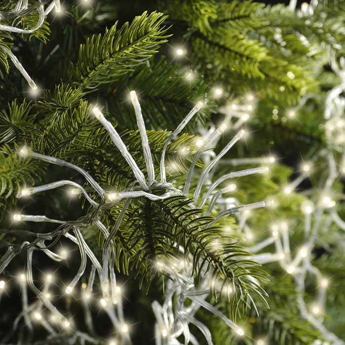 Close-up of green pine branches decorated with Cluster LED 768 ct. String Lights Warm White by Available for Pickup & Delivery, softly glowing and creating a festive holiday atmosphere.