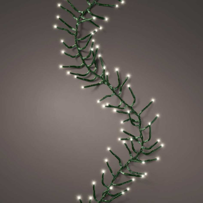 The Cluster Twinkle LED 500 ct. String Lights in Warm White from Available for Pickup & Delivery are lit, featuring small white bulbs draped in a loose, wavy pattern against a plain gray background.