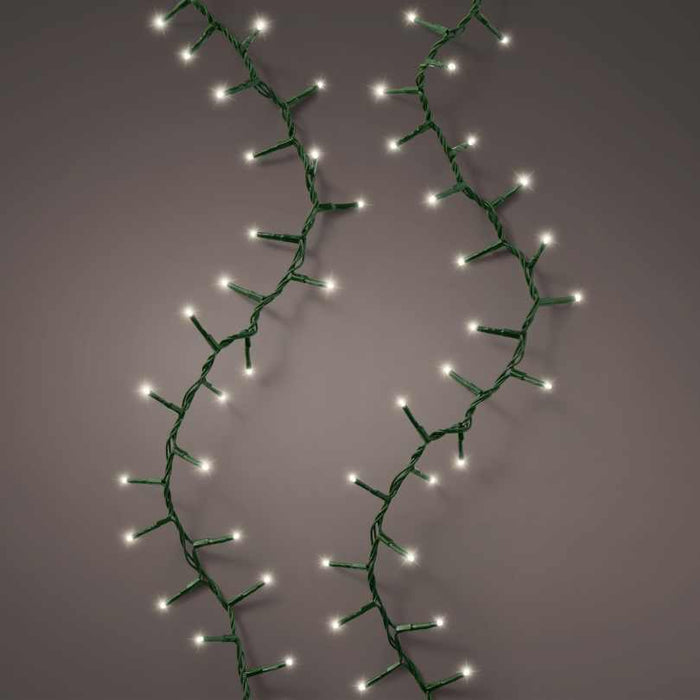Two strands of Compact Twinkle LED 500 ct. String Light Set Warm White by Available for Pickup & Delivery, featuring green wiring, are arranged in a loose zigzag pattern against a plain, neutral background.