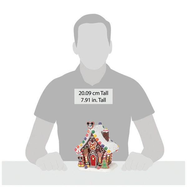 An illustration features Department 56 - Mickeys Gingerbread House, a festive masterpiece adorned with candy and frosting. This Christmas décor stands 20.09 cm (7.91 in) tall, embodying Mickeys playful charm. Available for Pick-Up & Delivery.