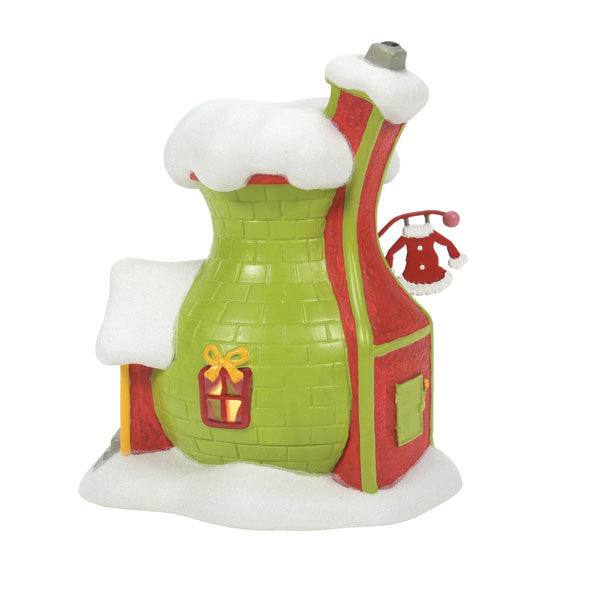 The Department 56 – Grinch’s Santy Suit Shoppe by Available for Pick-Up & Delivery is a whimsical, brightly colored ceramic house shaped like a green and red chimney with snow, featuring a small door, gift design window, and snowy Santy Suit hanging on the side—ideal for holiday décor.