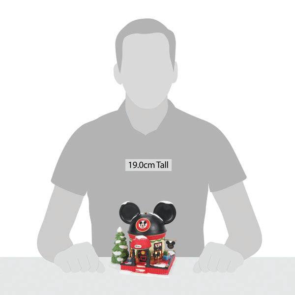 The Department 56 – Mickey Mouse Ear Hat Shop by Enesco Designed Giftware is a charming model house, featuring black Mickey Mouse ears and a chimney. Standing 19.0 cm tall, it includes holiday décor, a Christmas tree, and a dog figure to evoke Disneys whimsical magic at Christmastime.