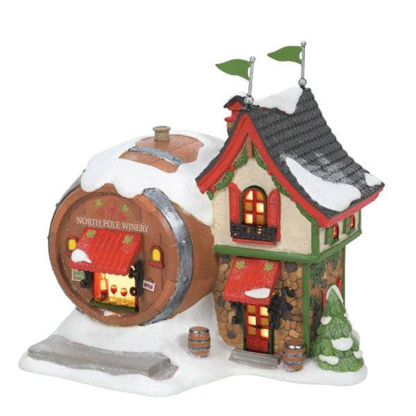 The Department 56 – North Pole Winery by Available for Pick-Up & Delivery is a charming Christmas décor piece. This miniature model displays a snowy red-roofed house with glowing windows and a barrel-shaped extension, adorned with snow and a small tree, offering a cozy festive atmosphere.
