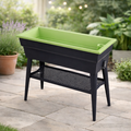 The Elevated Calipso Planter from Pickup & Local Delivery Only features a raised rectangular design with four legs and a perforated shelf below, perfect for your patio among potted plants and greenery.