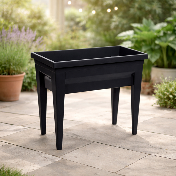 The Elevated Harvest Planter by Pickup & Local Delivery Only stands on a stone patio, surrounded by lush greenery and potted herbs, creating an inviting outdoor garden scene.
