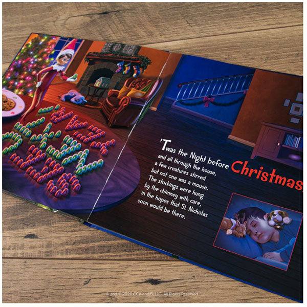 The Elf on the Shelf®: Night Before Christmas Book lies open on a wooden surface, revealing colorful scenes. On the left, Scout Elves by a tree with cookies and candy; on the right, a child sleeps warmly in bed, evoking classic Christmas charm. Available for Pick-Up & Delivery.