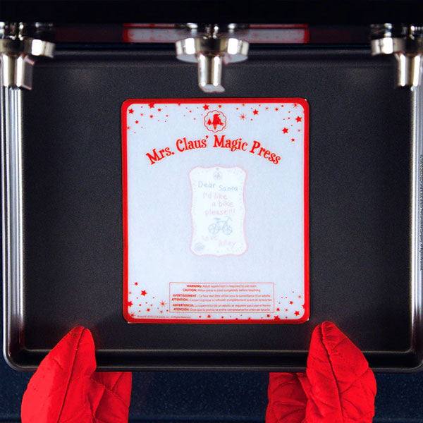 Red oven mitts hold a baking tray labeled Elf On The Shelf®: Scout Elf Express - Letters to Santa® Mini, featuring a festive design with stars and swirls that inspires children to craft elf-sized letters for Santa as part of this delightful Christmas activity kit.
