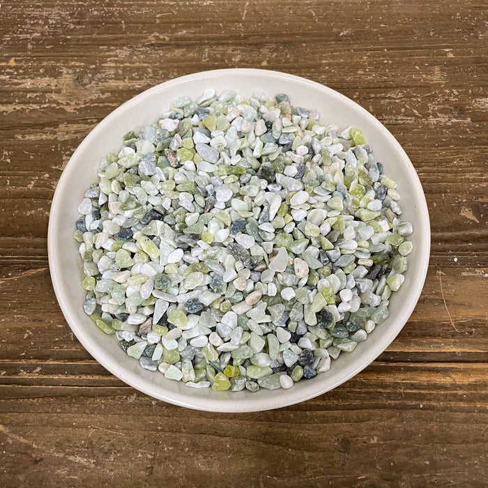 A white bowl holds Exotic Pebbles’ Jade Bean Pebbles (5 lb.)—small, polished stones in green, white, and gray—displayed on a brown wooden surface. Available for Pickup & Delivery.