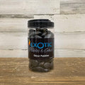 A clear plastic jar of Exotic Pebbles - Polished Black Pebble (5 lb.) from Available for Pickup & Delivery sits on a wooden surface with a light wood background—ideal as landscaping gravel or decorative stone.