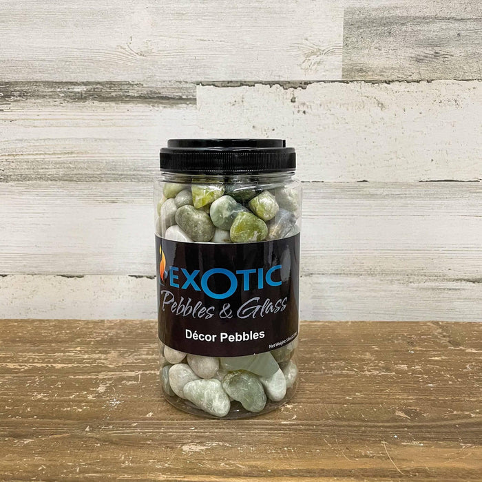 A clear jar labeled "Exotic Pebbles - Polished Jade Pebbles - 5 lb." by Available for Pickup & Delivery holds smooth, multicolored stones ideal for landscaping and is set on a wooden surface against a rustic, light wood background.