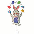 The Garden Stake – Juggling Bunny by Available for Pick-up & Delivery is a whimsical metal figure with long ears, a cheerful face, and a purple bowtie. It joyfully displays colorful eggs above its head and features a round body with a charming blue belly.