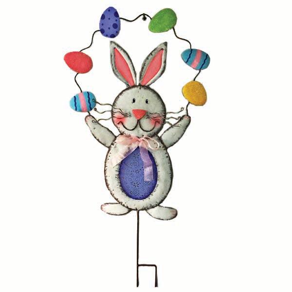 The Garden Stake – Juggling Bunny by Available for Pick-up & Delivery is a whimsical metal figure with long ears, a cheerful face, and a purple bowtie. It joyfully displays colorful eggs above its head and features a round body with a charming blue belly.