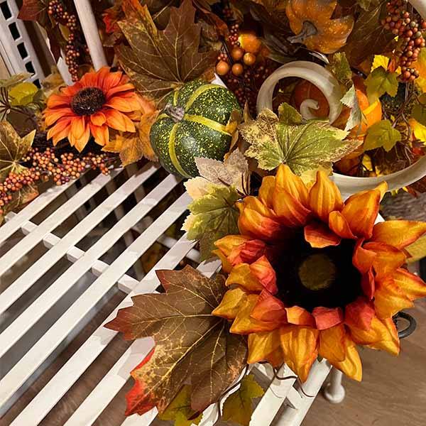 The Garland – Sunflowers & Pumpkins – 68” by Available for Pick-Up & Delivery is a cozy autumn decor with orange and yellow sunflowers, a small green pumpkin, and brown and green leaves on a white slatted shelf.