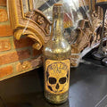 A vintage-style Halloween Bottle - Skull from Available for Pick-Up & Delivery, featuring a skull illustration, sits on a black surface near a cobweb-covered decorative mirror, making it perfect Halloween decor to enhance the eerie atmosphere.