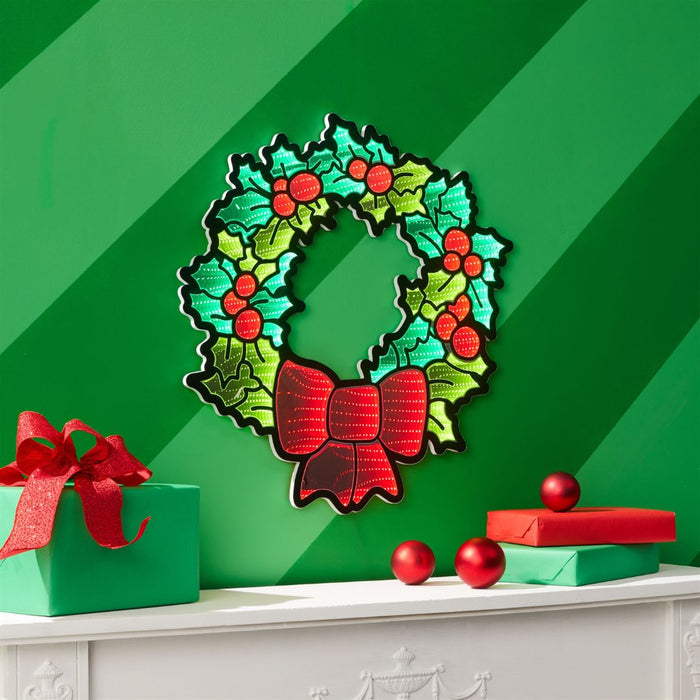 The Infinity Light – Holly Wreath - 24" from Available for Pick-Up & Delivery hangs above a white mantel on a green striped wall, bringing classic holiday charm with its festive design, perfect with gifts and red ornaments.