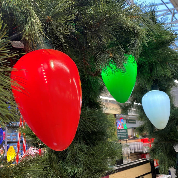 Jumbo LED Lit Bulbs in white by All Delivery Options hang from green artificial pine branches inside a store, with shelves and signs visible in the background.