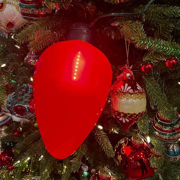 Jumbo red glowing retro-style Christmas bulb hanging on a Christmas tree at Hicks Nurseries.