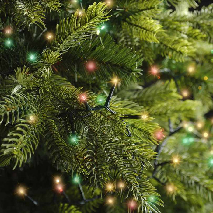 Close-up of green artificial pine branches decorated with LED 1000 ct. Compact String Lights Multi-Colored from Available for Pick-Up & Delivery, featuring vibrant red, green, and yellow bulbs for a festive, glowing look.