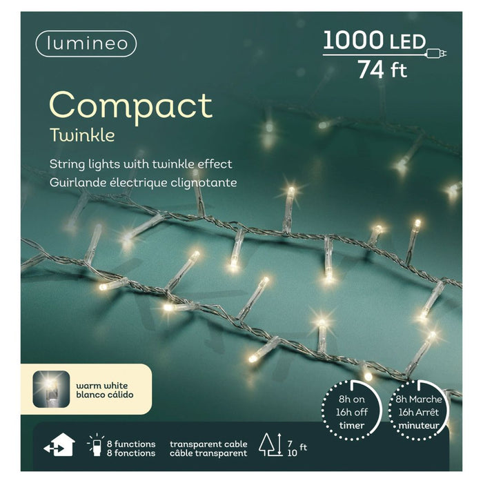 A close-up of LED 1000 ct. Compact String Lights Twinkle Warm White by Available for Pick-Up & Delivery on a greenish background. The 74 ft box highlights 8 functions, timer, transparent cable—perfect for outdoor holiday decor. English and French text shown.