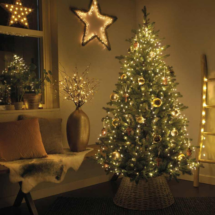 The Micro LED 672 ct. Tree Bunch Warm White from Available for Pick-Up & Delivery creates a festive holiday atmosphere, illuminating your Christmas tree with warm white LEDs and gold ornaments in a cozy, welcoming room.