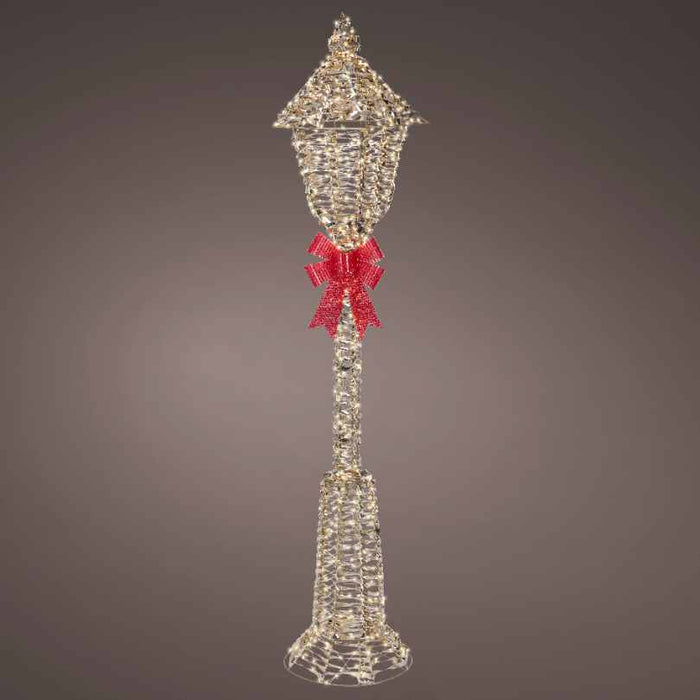 The Micro LED Lit Lamp Post with Red Bow – Warm White Lights from Available for Pick-Up & Delivery is a festive outdoor decoration, featuring micro LED lights and a large red bow, perfect for Christmas displays against any background.