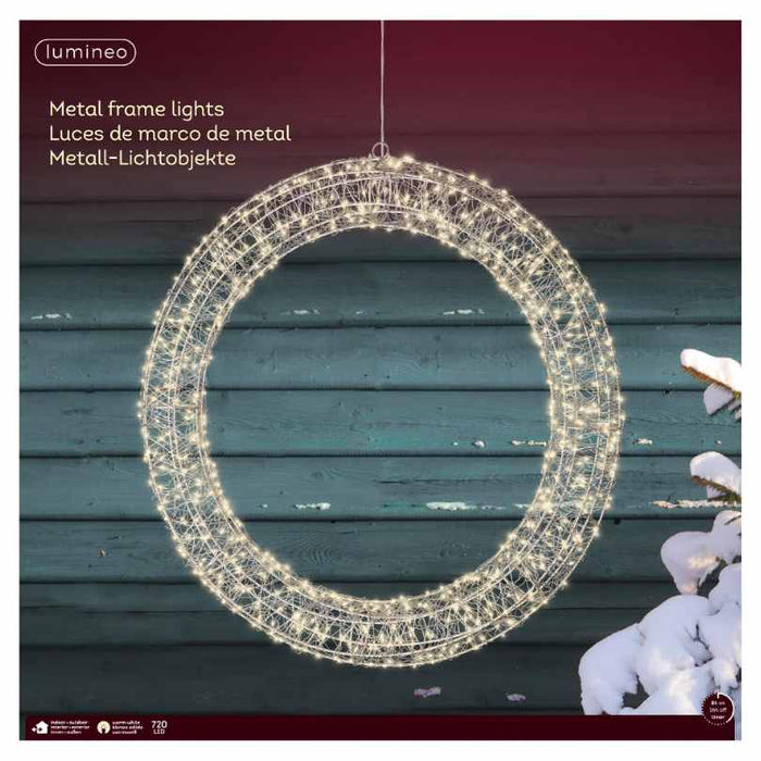 The Micro LED Lit Wreath - Warm White Lights - 23-Inch from Available for Pick-Up & Delivery adds cozy charm to your outdoor décor, glowing with warm LEDs against a blue wooden wall and snow-covered branches.