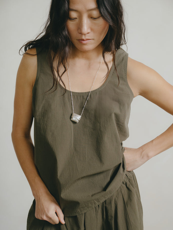 Woman wearing an olive green sleeveless top with a plain background