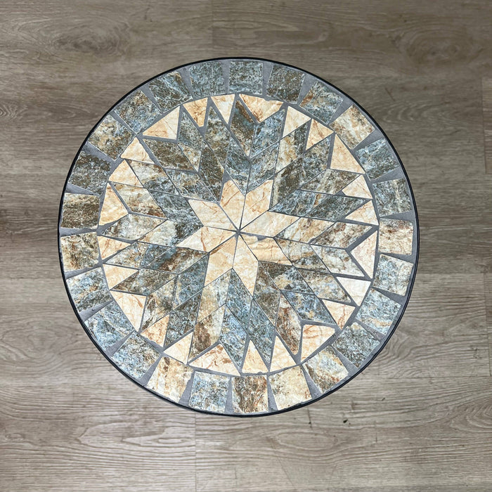 The Pickup & Local Delivery Only Plant Stand – Black Metal Mosaic Tile Sunburst – 23-inch features a round tabletop with a beige, gray, and brown geometric sunburst design on a sturdy black metal frame.