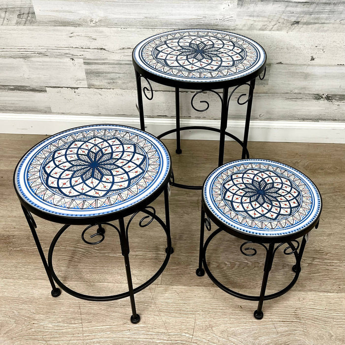 The All Delivery Options Plant Stand – Black Metal with Enamel Design (17) features round tops with blue, white, and orange patterns, sturdy curved legs, and suits indoor or outdoor use on any surface.