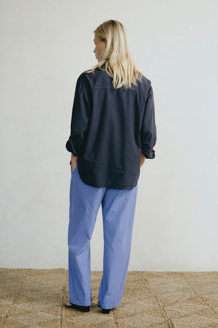 Person wearing a navy shirt and light blue pants standing against a plain background