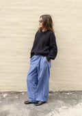 Person wearing a black sweater and blue pants standing against a beige wall.