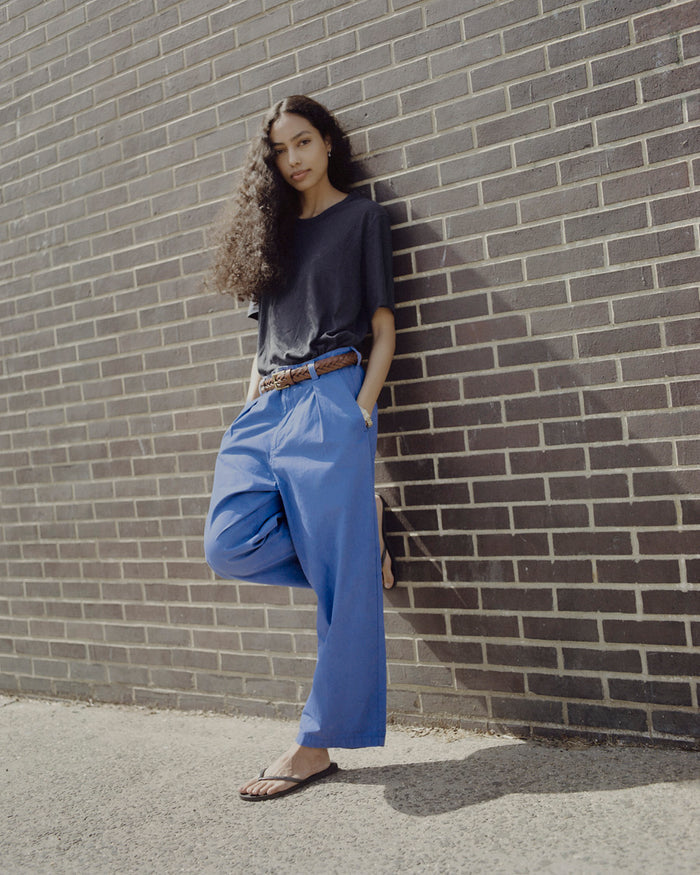 Person wearing a dark top and blue pants leaning against a brick wall.