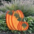 The Pumpkin Garden Stake - 34 by Available for Pick-Up & Delivery brings rustic charm to your garden. With an orange finish and green vine details, it sits elegantly among lush foliage and purple blooms, offering a perfect autumnal touch.