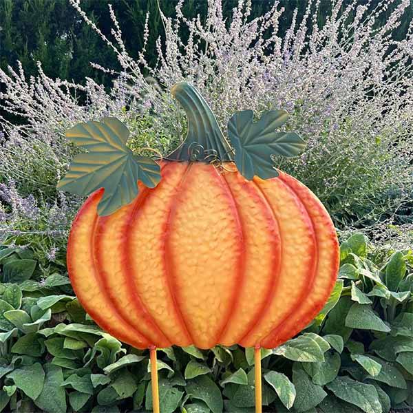 The Pumpkin Garden Stake – 32” by Available for Pick-Up & Delivery showcases a large, decorative pumpkin with vibrant orange hues and green leaves among lush lavender and greenery, adding rustic charm to your autumn garden decor.