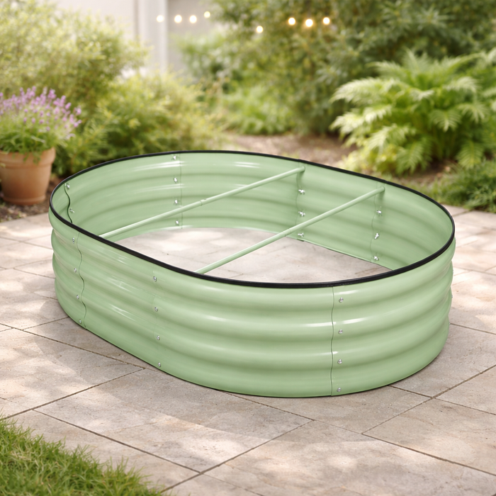 The Pick-Up & Local Delivery Only Raised Bed - Oval - Green, made of galvanized steel with a ribbed texture and internal support bars, sits on a stone patio surrounded by potted plants and greenery.