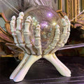The Skeleton Hands Holding Crystal Ball by Available for Pick-Up & Delivery features skeletal hands with a crystal ball against ornate vintage mirrors and cobwebs. Its perfect for creating a spooky Halloween ambiance.